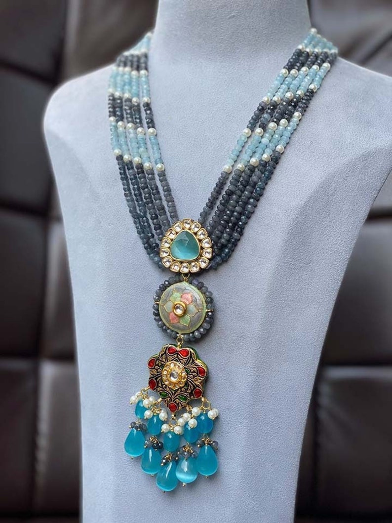 May include: A multi-strand necklace with blue and white beads and a large pendant with a floral design. The pendant is made of gold and has a blue stone in the center.