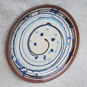 May include: A white ceramic plate with a brown rim and a blue and white spiral design. The plate has a crackled glaze and is decorated with blue and white dots.