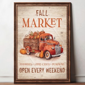May include: A framed print featuring a vintage red truck filled with pumpkins. The words "FALL MARKET" are displayed above the truck, with "HAYRIDES • APPLE CIDER • PUMPKINS" and "OPEN EVERY WEEKEND" below. The artwork has a rustic, autumnal theme.