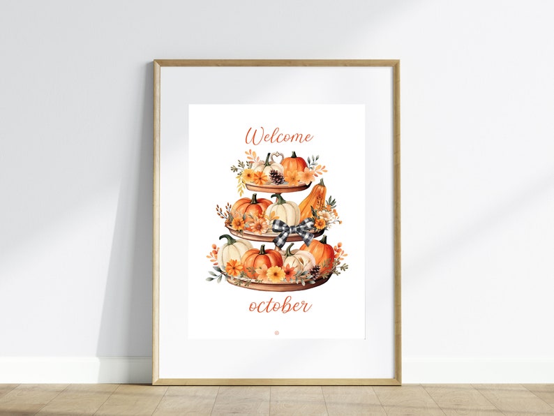 May include: A framed print featuring a watercolor illustration of a tiered tray filled with pumpkins, gourds, and fall foliage. The words "Welcome October" are written in a decorative font. The artwork is set against a white background.