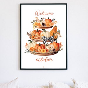 May include: A framed print featuring a tiered display of pumpkins, gourds, and flowers. The artwork has the words "Welcome" and "October" in orange script. A black and white checkered bow is in the center.