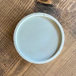 May include: A round, light gray concrete coaster with a smooth, slightly textured surface.