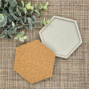 May include: Two hexagonal coasters, one made of cork and the other made of concrete. The cork coaster is brown and the concrete coaster is gray.