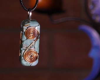 Può includere: Una collana con un ciondolo rettangolare in turchese e filo di rame. Il ciondolo è di forma rettangolare e presenta un filo di rame avvolto attorno a pietre turchesi.