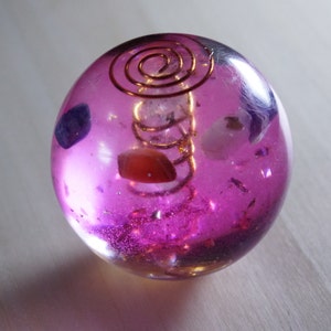Può includere: Una sfera trasparente rosa con una spirale di filo di rame all'interno. La sfera contiene vari piccoli cristalli, tra cui ametista, quarzo rosa e quarzo trasparente.