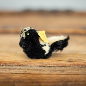 May include: A black and white stuffed skunk with a yellow tag. The skunk is lying on a wooden surface.