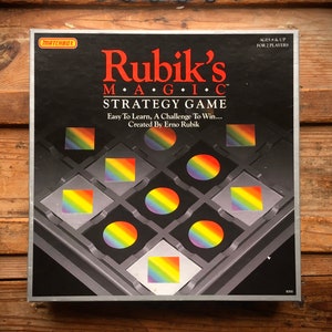 May include: A black box game with a rainbow design. The box features the text "Rubik's MAGIC STRATEGY GAME" and "Easy To Learn, A Challenge To Win... Created By Erno Rubik".
