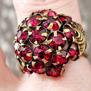 Può includere: Un anello d'oro con un grande gruppo di strass rosso scuro. L'anello è ornato e in stile vintage.