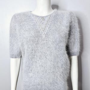 May include: A grey fuzzy sweater with short sleeves and a sparkly, geometric design on the neckline.