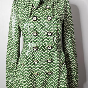 May include: Green and white geometric pattern double-breasted coat with black and white buttons. The coat has a collared neckline and long sleeves. The coat is displayed on a mannequin.