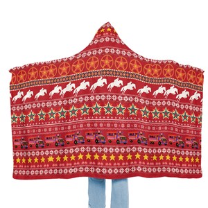 May include: Red hooded blanket with a festive pattern featuring stars, horses, and trucks. The blanket is made of soft fleece and is perfect for staying warm on cold nights.