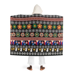 Puede incluir: Una manta con capucha con fondo negro y un patrón colorido con estrellas, soles y banderas. El patrón recuerda a los diseños tradicionales filipinos.