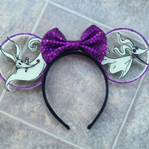May include: Purple glitter Minnie Mouse ears with a white and black image of Zero, the ghost dog from The Nightmare Before Christmas, on each ear.