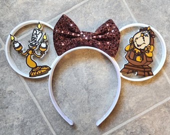 May include: White headband with brown glitter bow and two white ears. One ear features a yellow and white cartoon of Lumiere from Beauty and the Beast. The other ear features a yellow and brown cartoon of Cogsworth from Beauty and the Beast.