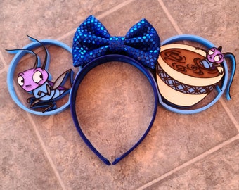 May include: Blue and white Mickey Mouse ears with a blue bow, a cartoon bug, and a cup of tea with a cartoon bug on top.