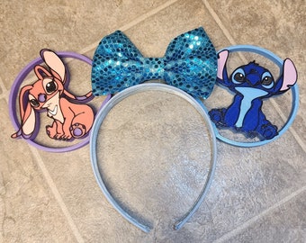 May include: A pair of blue and purple mouse ears with a blue sparkly bow. The ears feature Stitch and Angel from the Disney movie Lilo & Stitch.