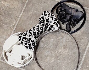 May include: A pair of black and white Star Wars themed Minnie Mouse ears. The ears are shaped like Darth Vader and a Stormtrooper. The headband is gray.