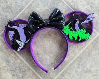 May include: Purple and black mouse ears with a green and purple dragon design. The ears are decorated with black sequins and a purple bow.