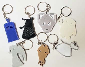 May include: A set of eight keychains featuring various characters from the Doctor Who television series. The keychains are made of white, black, blue, and brown plastic and feature characters such as the Dalek, the TARDIS, and the Weeping Angels.