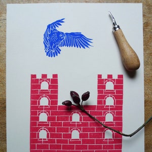 May include: A blue bird flying over a red brick castle with a branch of red berries in front of it.