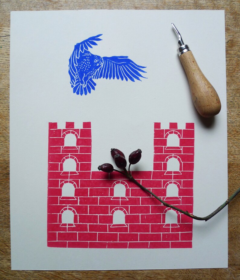 May include: A blue bird flying over a red brick castle with a branch of red berries in front of it.