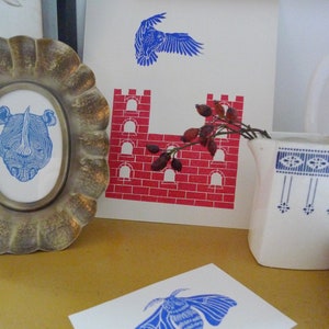 May include: A set of three blue and red prints featuring a bird, a castle, and a moth. The prints are on white paper and are framed in a simple white frame.
