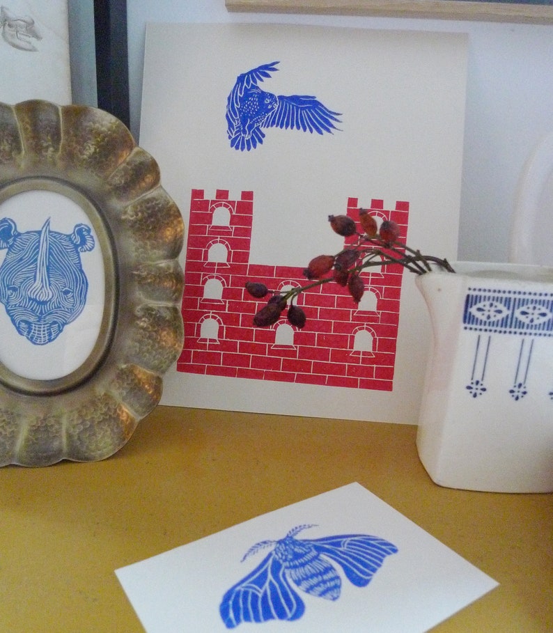 May include: A set of three blue and red prints featuring a bird, a castle, and a moth. The prints are on white paper and are framed in a simple white frame.