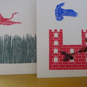 May include: Two pieces of art, one with a red bird flying over a green field and the other with a red brick castle with a branch of red berries.