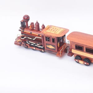 May include: A wooden toy train set with a brown engine and a passenger car. The engine has a brown and gold paint scheme with intricate details. The passenger car has a brown roof and windows.