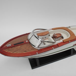 May include: A white and red wooden model boat with a brown interior and a small Italian flag on the back. The boat is on a black stand.