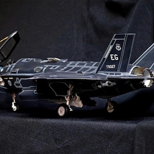 May include: A black and gray model of a fighter jet with the text "EG 15027" on the side.