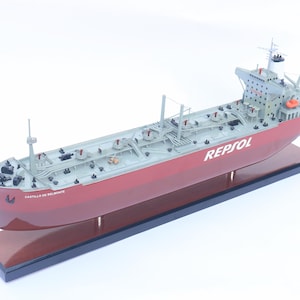 Pode incluir: Um modelo de navio tanque vermelho e cinza com o nome "CASTILLO DE BELMONTE" e o logotipo "REPSOL" no lado. O navio está em uma base de madeira.