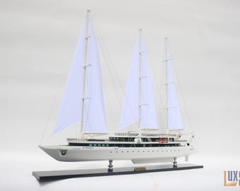 Puede incluir: Maqueta de velero blanco con tres mástiles y velas blancas. El modelo está montado sobre una base negra. El barco es una réplica del yate de vela Le Ponant.