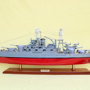 Könnte beinhalten: Ein detailliertes Modell des Schlachtschiffs USS Arizona, ein graues und rotes Schiff mit einem Holzsockel. Der Sockel trägt den Text "USS ARIZONA".