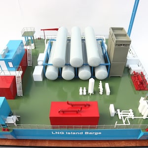 May include: A detailed model of an LNG Island Barge, featuring blue, red, and white structures. The model includes cylindrical tanks, piping, and the text "LNG Island Barge" on the side. The barge is set on a green deck.