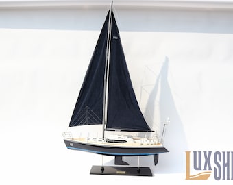 Puede incluir: Un modelo de velero en blanco y negro con una vela negra y una línea de flotación azul. El modelo está sobre un soporte negro con una placa de identificación que dice "SAIL".