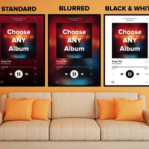 May include: Three framed music art prints with a modern design. Each print features a music player interface with the text "Choose ANY Album". The prints are displayed above a beige sofa with orange cushions.