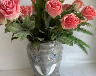 Puede incluir: Un ramo de rosas rosas en un jarrón de elefante de cerámica gris.