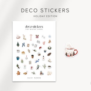 May include: A sheet of stickers featuring a variety of winter-themed illustrations, including a mug of hot cocoa, a snowman, a gingerbread man, and a Christmas tree. The stickers are labeled "Deco Stickers Tiny Winter Things Daily Papers".