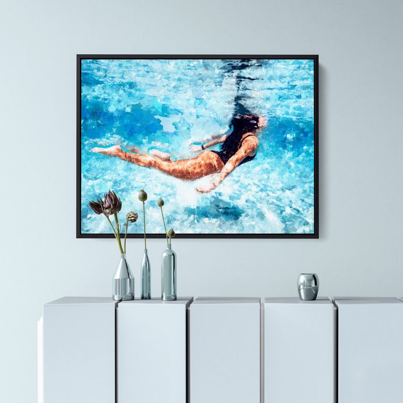May include: A framed watercolor painting of a person swimming underwater in a pool. The water is a light blue color and the person is wearing a black swimsuit. The painting is framed in a black frame.