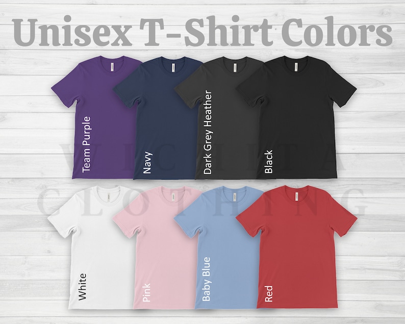 May include: A selection of unisex t-shirts in various colors, including white, team purple, navy, dark grey heather, black, pink, baby blue, and red. The shirts are displayed on a white wood background. Unisex T-Shirt Colors