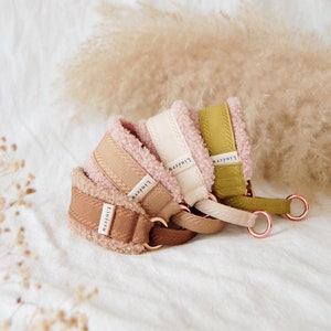May include: Three dog collars in different colours and textures. The collars are made of a soft, fuzzy material and have a brown, beige, and green colour. Each collar has a metal ring and the word "Linecru" printed on it.