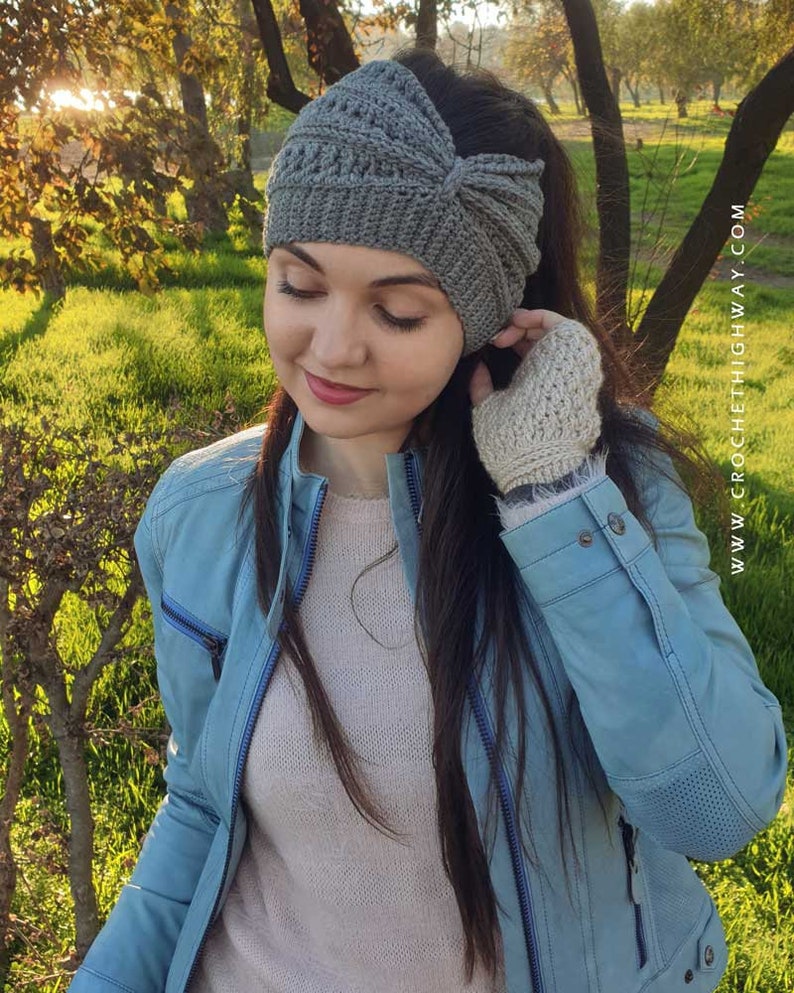 May include: A gray crocheted headband with a knot on the top. The headband is worn by a person with long brown hair. The person is wearing a light blue jacket and a light pink sweater.