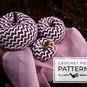 May include: Three crocheted pumpkins in a chevron pattern, with the largest pumpkin in purple and white, the medium pumpkin in purple and white, and the smallest pumpkin in white and purple. The pumpkins are sitting on a pink fabric surface. The text "CROCHET PDF PATTERN by Crochet Highway" is in a white box on the bottom right of the image.