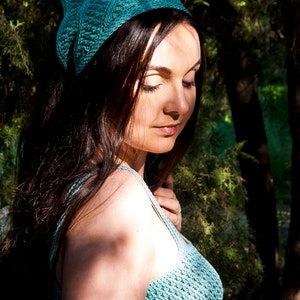 Puede incluir: Una mujer con una diadema de ganchillo turquesa y un top de ganchillo turquesa. La mujer est&aacute; de pie en un bosque con &aacute;rboles verdes y la luz del sol brillando a trav&eacute;s de las hojas.