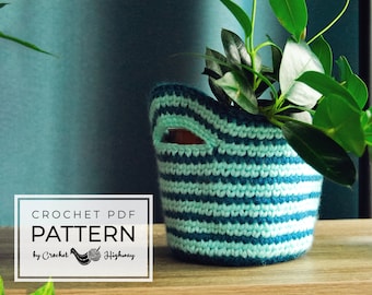 May include: Crochet PDF Pattern by Crochet Highway. A teal and light blue striped crocheted plant pot with a plant inside.