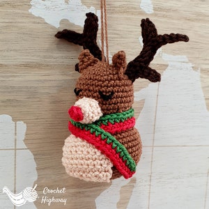 Peut inclure: Une d&eacute;coration de No&euml;l en forme de renne crochet&eacute; avec un nez rouge, des bois bruns et une &eacute;charpe verte et rouge. La d&eacute;coration est suspendue &agrave; une ficelle.