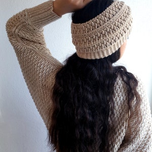 May include: A beige crochet headband with a textured pattern. The headband is worn by a person with long, dark hair.