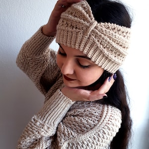 May include: A beige crocheted headband with a knotted design. The headband is worn by a person with long dark hair.