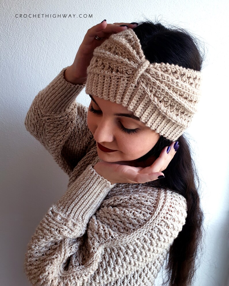 May include: A beige crocheted headband with a knotted design. The headband is worn by a person with long dark hair.